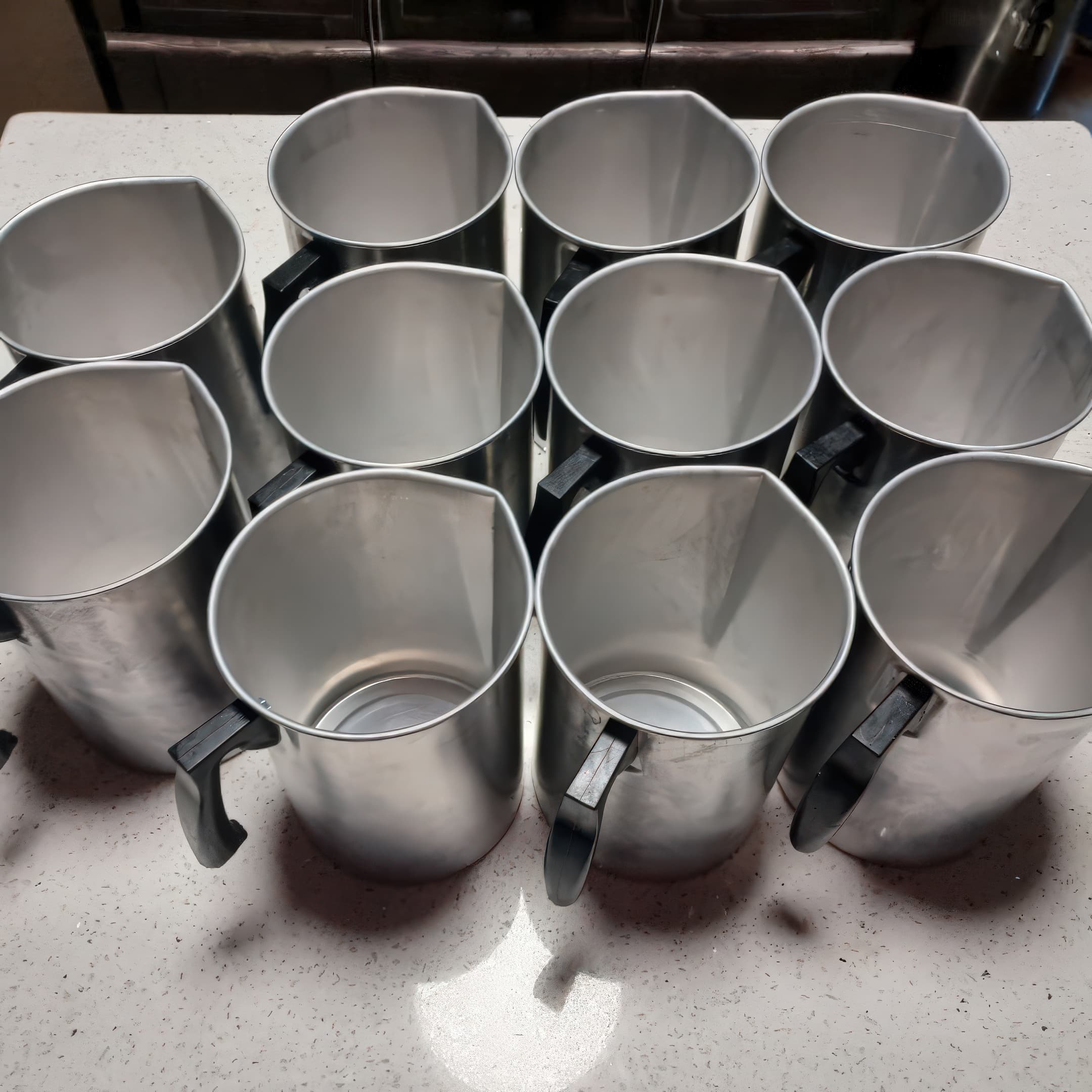 Top-down view of stainless steel pouring pitchers lined up on a countertop during the blending process